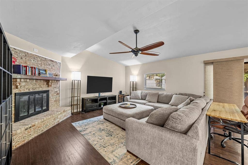Living area featuring a floor-to-ceiling stone-faced fireplace with a natural wood mantel, wood-finish flooring, vaulted ceilings, and a multi-blade ceiling fan