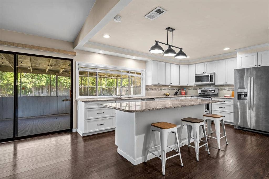 Kitchen featuring a central island with stone-finish countertops, white cabinetry with dark hardware, stainless steel appliances, wood-finish flooring, and a sliding glass door