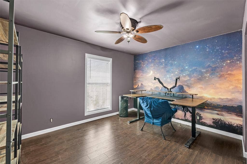 Wood-finish flooring, ceiling fan with integrated lighting, window with horizontal blinds, and accent wall featuring landscape imagery