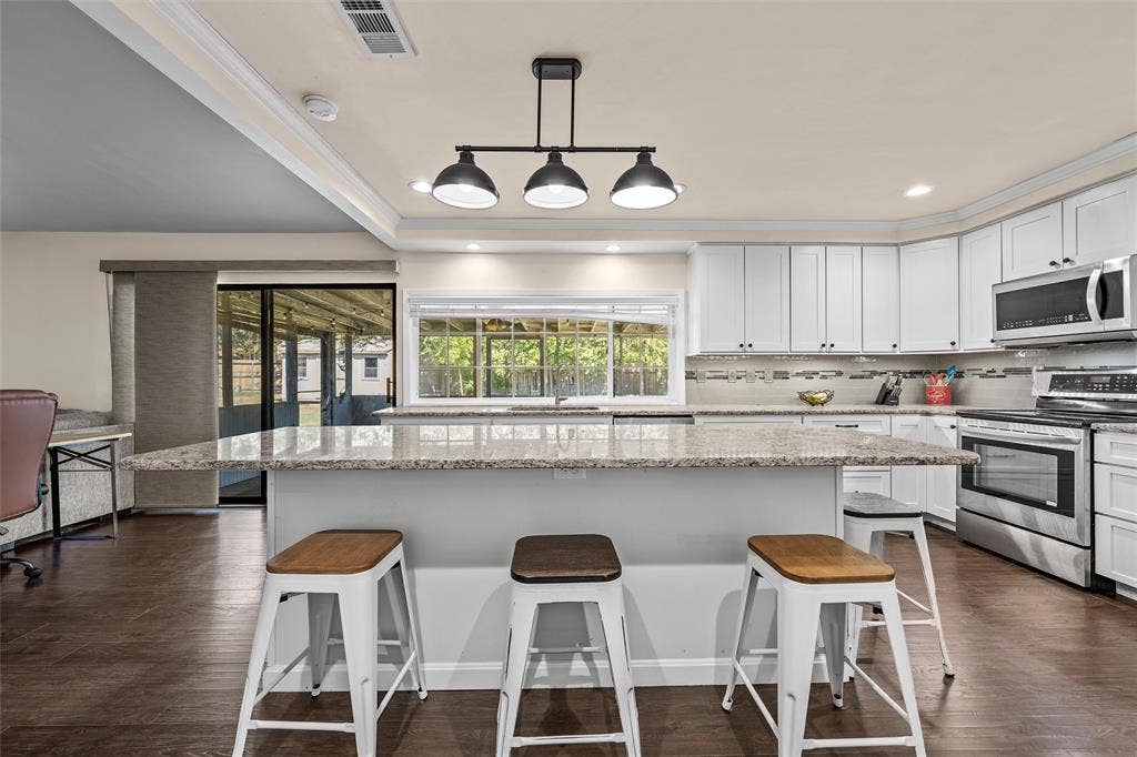 Kitchen featuring a stone-topped island with seating, white cabinetry, stainless steel appliances, and a three-light pendant fixture over wood-finish flooring