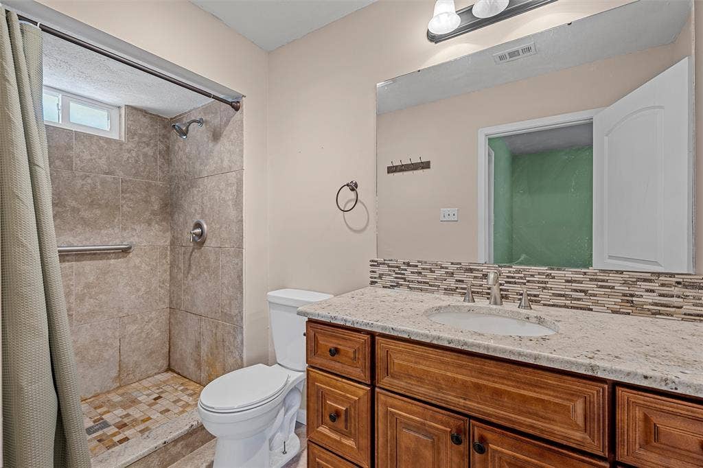 Bathroom featuring a stone-topped vanity with wood-finish cabinetry, a tiled walk-in shower with mosaic flooring, and a large wall-mounted mirror with a decorative tile backsplash