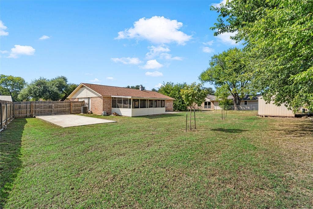 Spacious backyard featuring a grass lawn, enclosed patio, concrete slab, wood-style fencing, and a detached storage shed