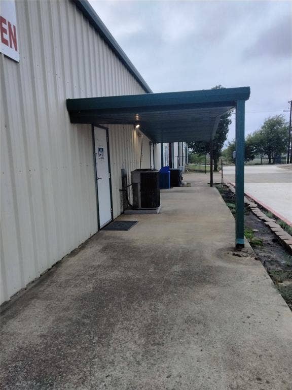 Exterior metal-clad siding featuring a covered concrete walkway, steel support posts, and external utility units