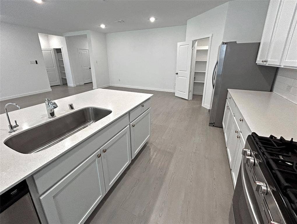 2504 Clyde Road, Celina, TX 75009 Kitchen featuring a central island with a stainless steel under-mount sink, quartz countertops, white shaker-style cabinetry, gas range, and luxury vinyl plank flooring