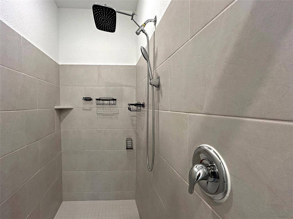 2504 Clyde Road, Celina, TX 75009 Walk-in shower featuring large-format ceramic tile surround, integrated rainfall showerhead, handheld shower wand, and polished chrome hardware