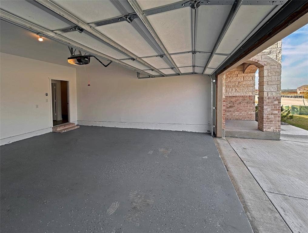 2504 Clyde Road, Celina, TX 75009 Garage featuring an epoxy-coated concrete floor, an overhead automatic door opener, and finished interior walls