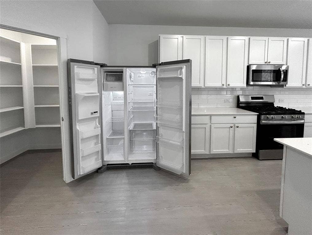 2504 Clyde Road, Celina, TX 75009 Kitchen featuring white shaker-style cabinetry, a subway tile backsplash, light-colored countertops, stainless steel appliances with a refrigerator, and a walk-in pantry with built-in shelving