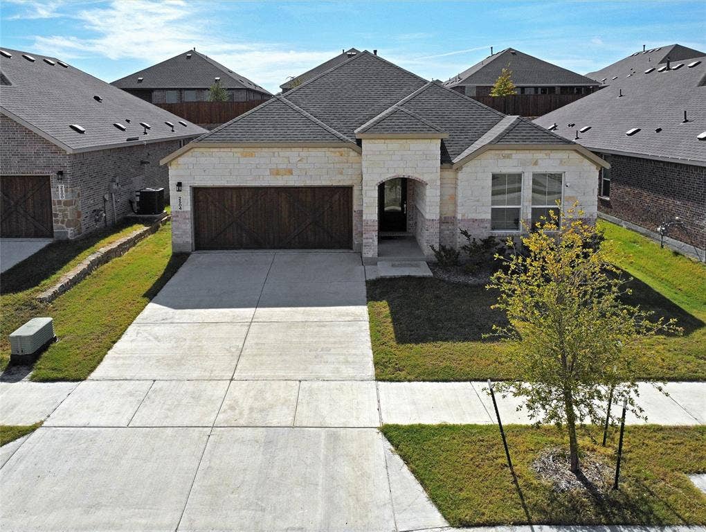 2504 Clyde Road, Celina, TX 75009 Stone veneer exterior features a dual-car garage with wood-finish decorative doors, asphalt shingle roofing, and a concrete driveway