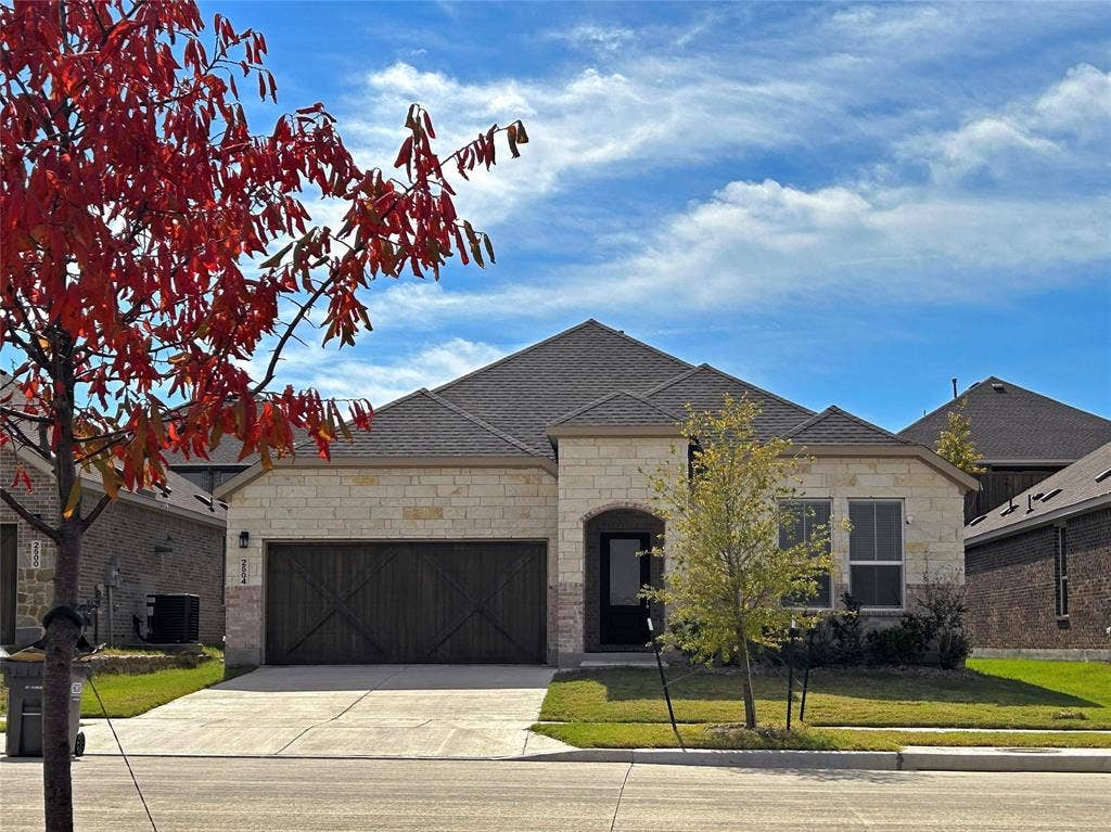 2504 Clyde Road, Celina, TX 75009 Single-story stone veneer exterior featuring a multi-gabled roofline, dark-toned carriage-style garage door with X-brace detailing, and a covered entryway