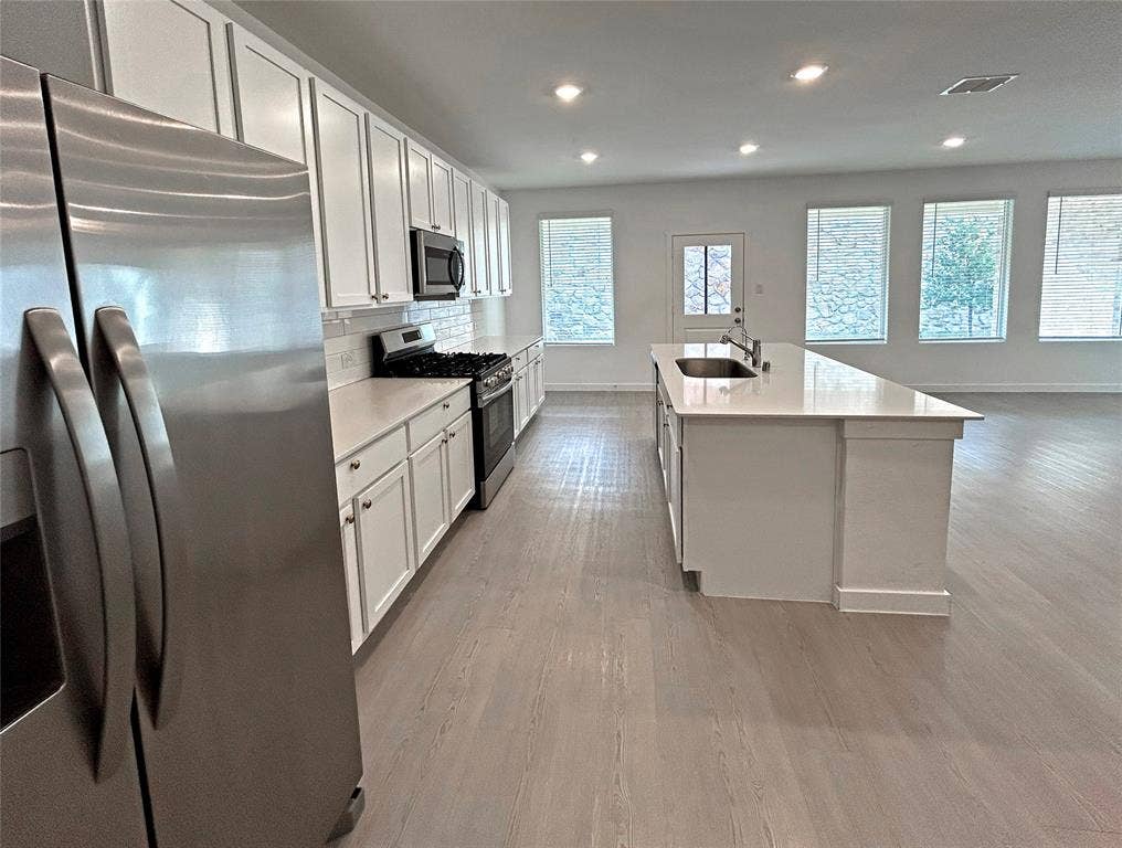 2504 Clyde Road, Celina, TX 75009 Kitchen featuring white cabinetry, solid-surface countertops, center island with undermount sink, stainless steel appliances, and luxury vinyl plank flooring