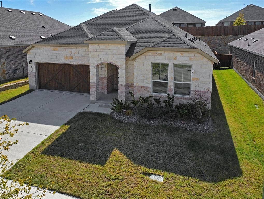 2504 Clyde Road, Celina, TX 75009 Stone veneer exterior, architectural shingle roof, arched covered entryway, and decorative wood-finish garage door with cross-buck detailing