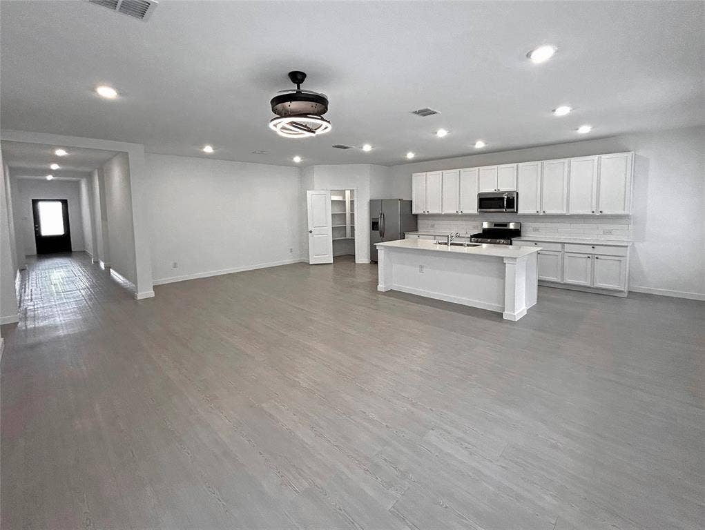 2504 Clyde Road, Celina, TX 75009 Open-concept interior featuring luxury vinyl plank flooring, recessed lighting, a kitchen island with stone countertop, white shaker-style cabinetry, and an enclosed pantry