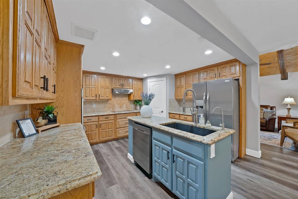 306 E Rochelle Boulevard, Irving, TX 75062 Kitchen featuring wood cabinetry, stone countertops, a contrasting blue center island with a drop-in sink, recessed lighting, and wood-finish flooring