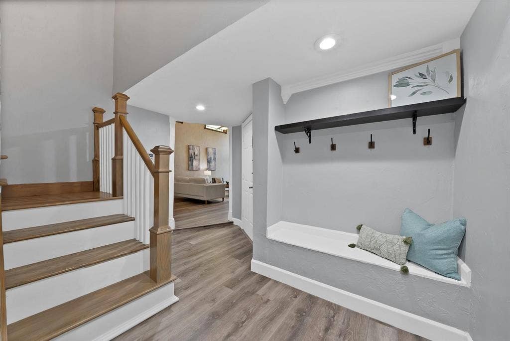 306 E Rochelle Boulevard, Irving, TX 75062 Entryway featuring wood-finish flooring, a built-in bench, wall-mounted coat hooks with a floating shelf, and a staircase with wood handrails and white balusters