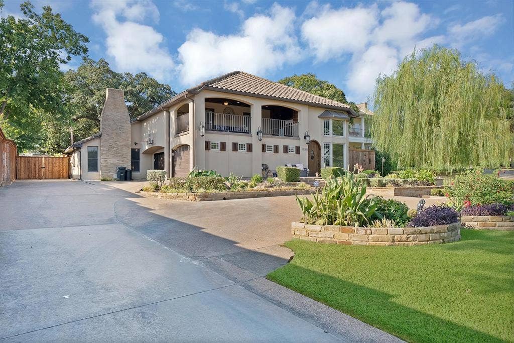 306 E Rochelle Boulevard, Irving, TX 75062 Stucco exterior featuring a second-story covered balcony, tile roof, exterior stone-finish chimney, and tiered stone landscaping walls