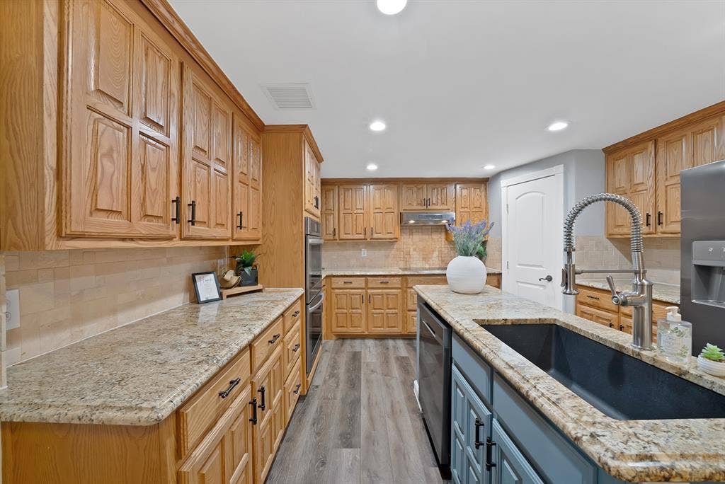 306 E Rochelle Boulevard, Irving, TX 75062 Kitchen featuring stained wood cabinetry, stone countertops, integrated wall oven, wood-finish flooring, and an undermount sink with a pull-down faucet