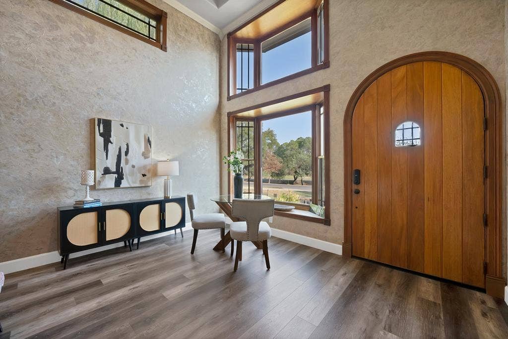 306 E Rochelle Boulevard, Irving, TX 75062 Vaulted ceiling foyer featuring a custom arched solid wood entry door, expansive bay windows, textured wall finishes, and wide-plank wood-finish flooring