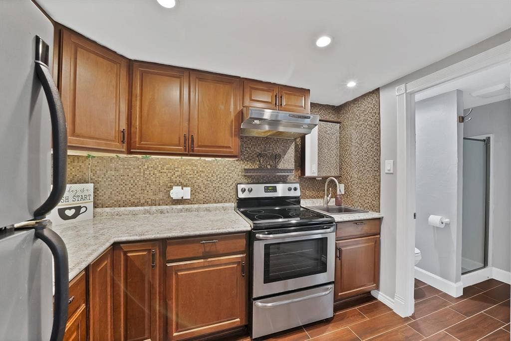 306 E Rochelle Boulevard, Irving, TX 75062 Kitchen featuring stained wood cabinetry, stone-finish countertops, textured tile backsplash, stainless steel range with overhead vent hood, and wood-finish flooring