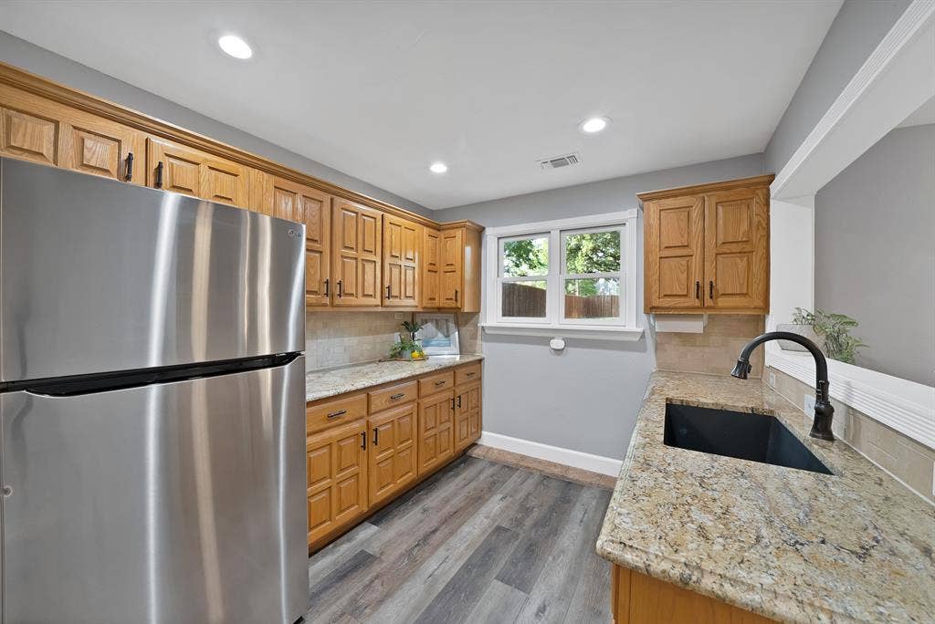 306 E Rochelle Boulevard, Irving, TX 75062 Kitchen featuring wood cabinetry, natural stone countertops, a stainless steel refrigerator, recessed lighting, and a black undermount sink with a gooseneck faucet