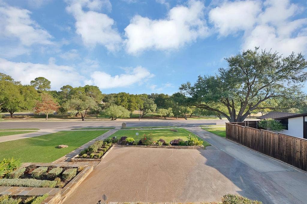 306 E Rochelle Boulevard, Irving, TX 75062 Concrete driveway, tiered stone-bordered landscaping, manicured lawn, and wood-finish perimeter fencing