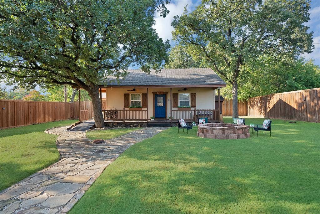 306 E Rochelle Boulevard, Irving, TX 75062 Exterior facade featuring a covered front porch, stone-paved walkway, fire pit, mature trees, and wood-panel privacy fencing