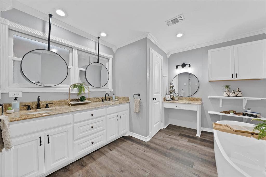 306 E Rochelle Boulevard, Irving, TX 75062 Dual-vanity cabinetry with stone countertops, suspended circular mirrors, wood-finish flooring, built-in vanity station, and wall-mounted shelving