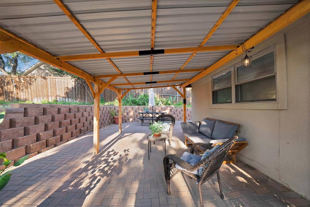 306 E Rochelle Boulevard, Irving, TX 75062 Covered outdoor patio featuring a metal roof, wood-frame support beams, interlocking paver flooring, and a tiered stone retaining wall
