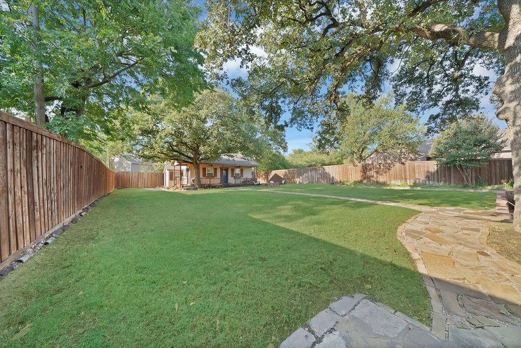 306 E Rochelle Boulevard, Irving, TX 75062 Expansive backyard featuring a large grass lawn, perimeter wood fencing, flagstone path, and mature shade trees