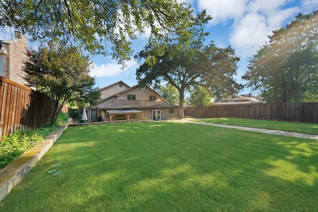 306 E Rochelle Boulevard, Irving, TX 75062 Expansive backyard featuring a level lawn, stone retaining walls, stone-paved walkway, wood privacy fencing, and mature canopy trees