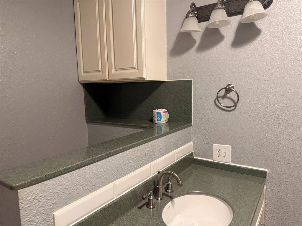 Stone-surfaced countertop with an integrated basin, white subway tile backsplash, wall-mounted cabinet, and three-bulb vanity fixture