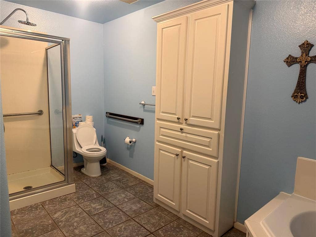 Bathroom featuring a tiled walk-in shower with chrome hardware, tall built-in cabinetry with shaker-style doors, and ceramic tile flooring