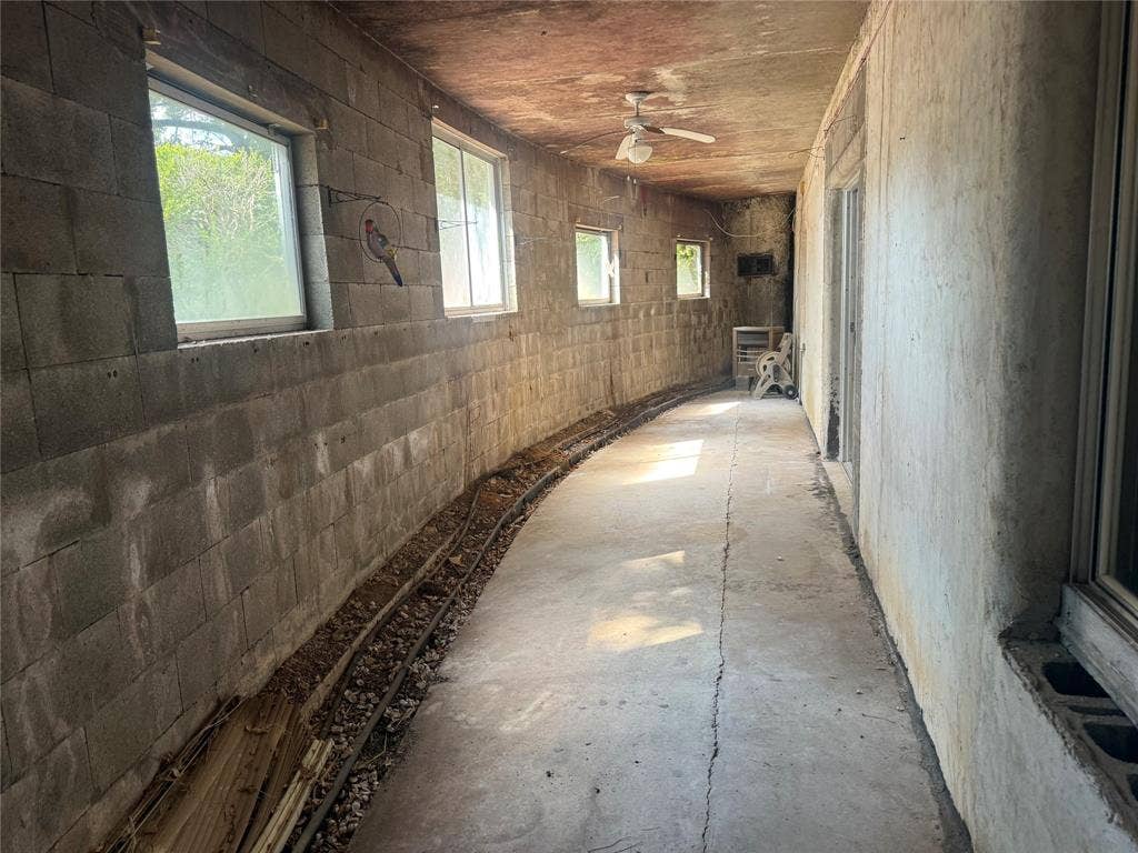 Enclosed area featuring concrete masonry unit walls, a concrete floor, four windows, and an overhead ceiling fan