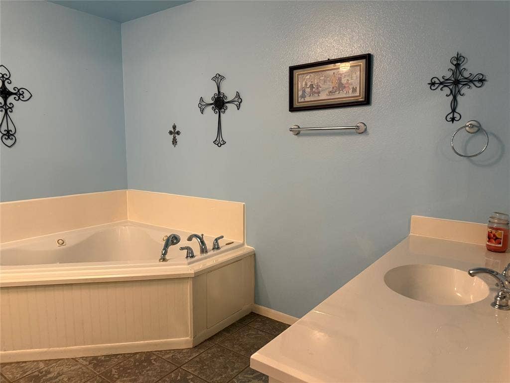 Corner soaking tub and apron, complemented by a white countertop, vanity sink with metal faucet, and installed towel hardware