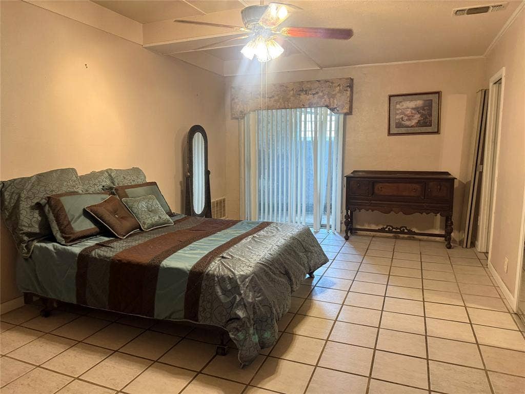 Interior space featuring large-format square tile flooring, ceiling fan with integrated light fixture, and floor-to-ceiling sliding glass doors with a decorative fabric valance