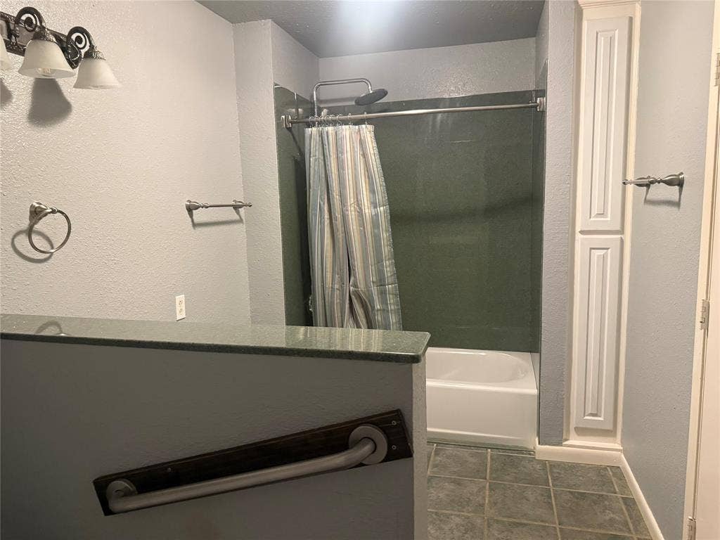 Bathroom featuring a built-in floor-to-ceiling storage cabinet, solid-surface partition countertop, tile flooring, and tub-shower combination with surround