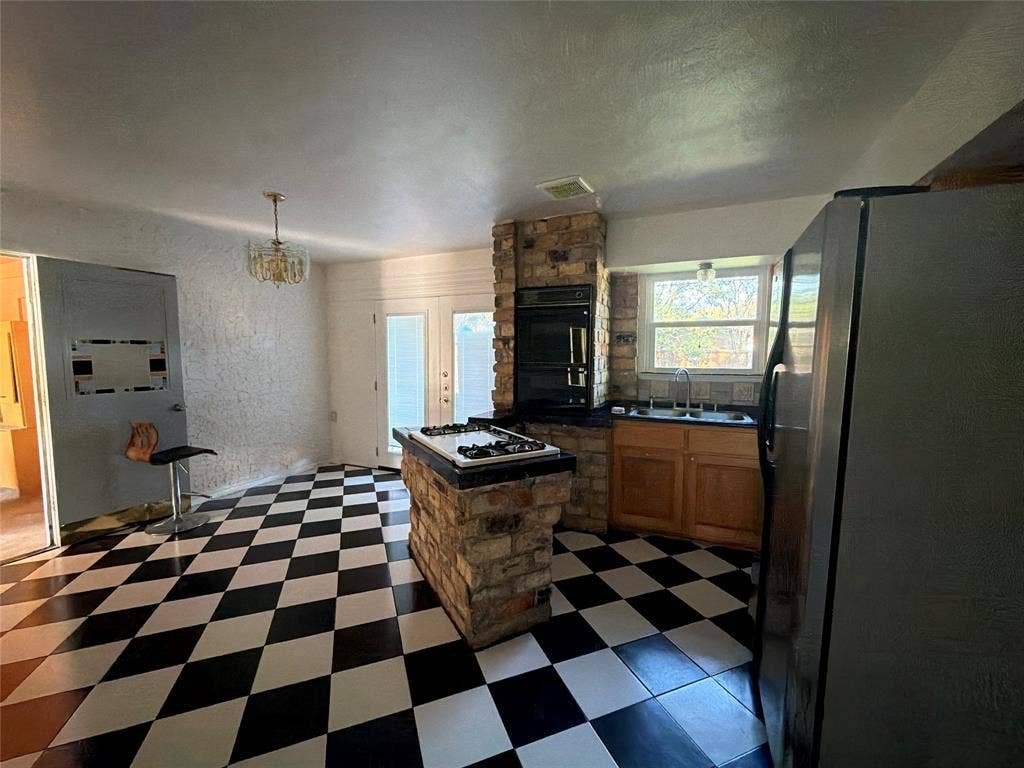 1819 Finley Road, Irving, TX 75062 Kitchen featuring a prominent stone-clad central island with an integrated cooktop, double wall ovens, wood cabinetry, and a checkered tile floor