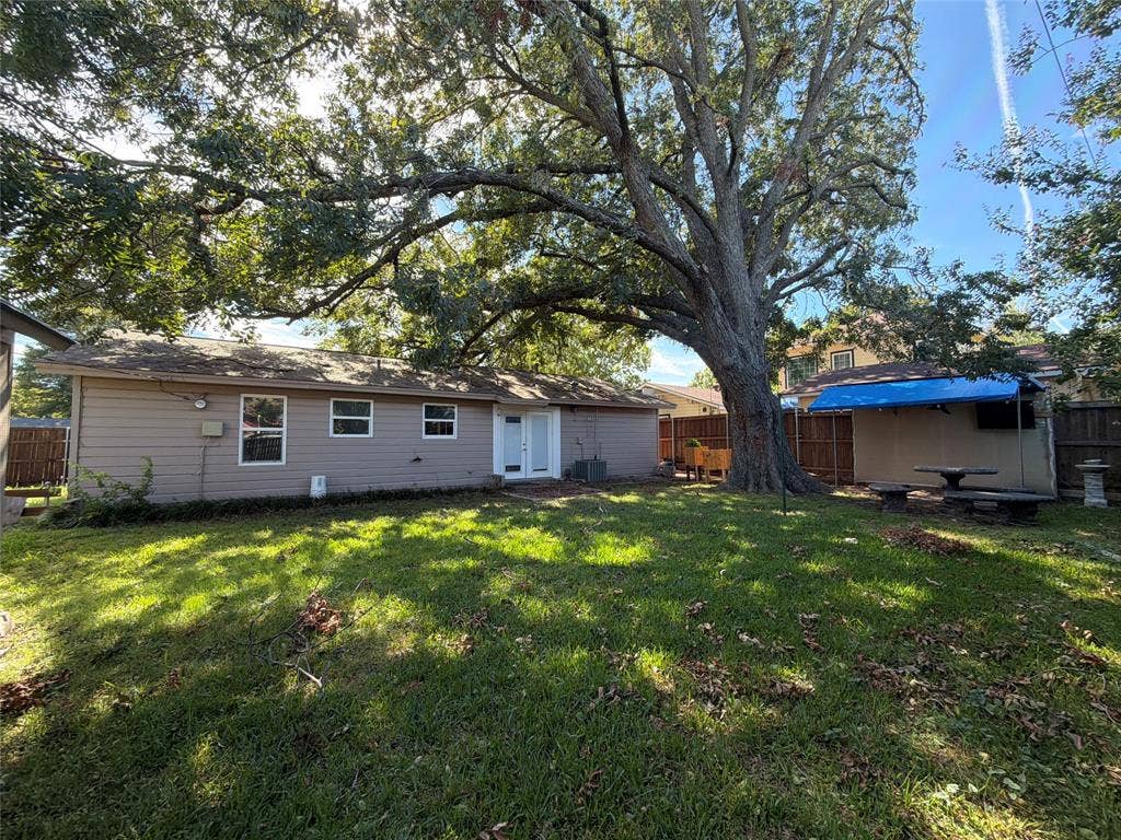 1819 Finley Road, Irving, TX 75062 Expansive backyard featuring a mature canopy tree, wood-paneled exterior siding, a covered patio structure, and perimeter privacy fencing