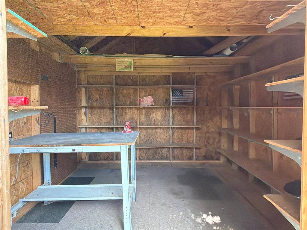 1819 Finley Road, Irving, TX 75062 Storage structure featuring extensive built-in wooden shelving, a metal-framed workbench, and exposed timber-frame construction