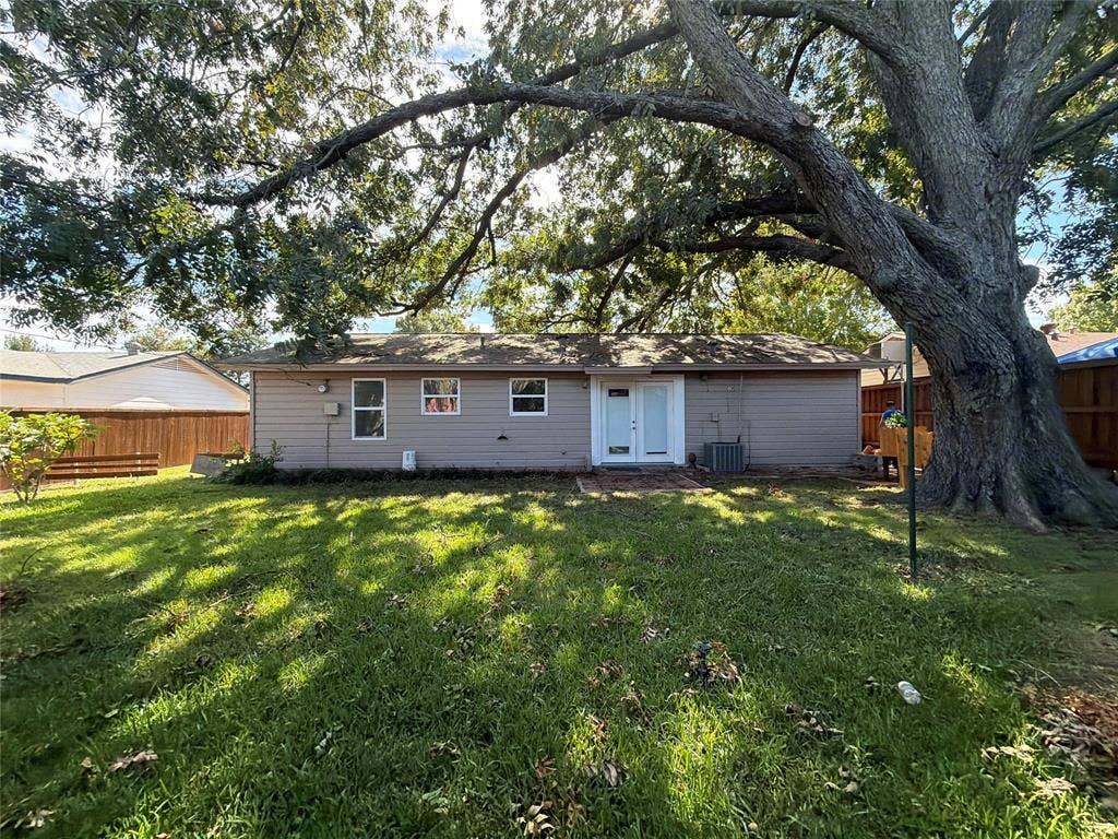 1819 Finley Road, Irving, TX 75062 Rear exterior featuring horizontal siding, double glass-paneled entry doors, a mature tree, and wood privacy fencing