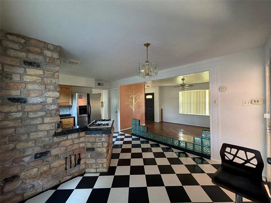 1819 Finley Road, Irving, TX 75062 Interior space featuring a floor-to-ceiling multi-tonal brick fireplace, black-and-white checkered flooring, decorative glass block partitions, wood-finish flooring, and a multi-arm brass chandelier