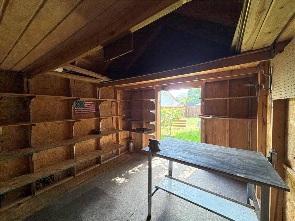 1819 Finley Road, Irving, TX 75062 Outbuilding featuring wood-paneled walls, multiple rows of built-in shelving, vaulted ceiling, and a stationary workbench