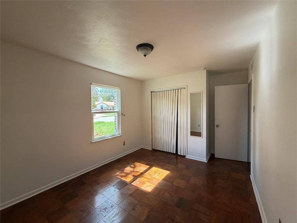 1819 Finley Road, Irving, TX 75062 Interior room featuring parquet wood-finish flooring, a double-door closet with vertical sliding panels, a wall-mounted mirror, a single-pane window, and a central ceiling-mounted light fixture