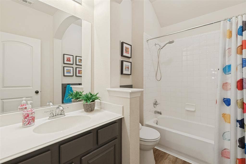 Bathroom featuring a dark-toned vanity cabinet with a light-colored countertop, integrated oval sink, chrome-finish faucet, and a combination tub-shower with white tile surround
