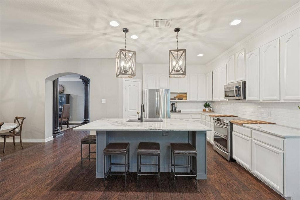 Kitchen featuring white cabinetry, stone-surface central island with integrated sink, stainless steel appliances, wood-finish flooring, and pendant lighting