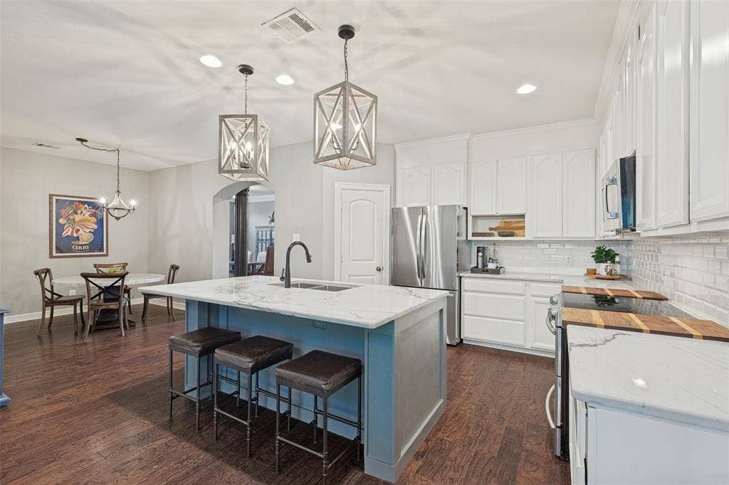 Kitchen featuring white cabinetry, a center island with a Quartzite countertop, stainless steel appliances, geometric pendant lighting, and wood-finish flooring