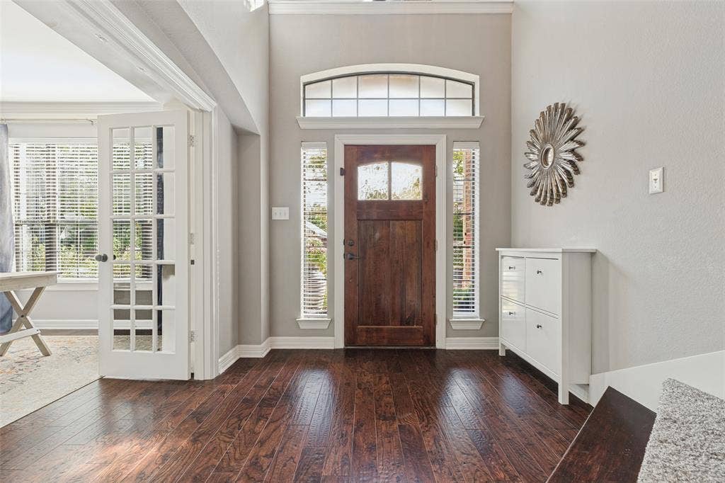 Entryway featuring dark-stained wood-finish flooring, a solid wood front door with a glass inlay, a transom window, and white-painted French doors