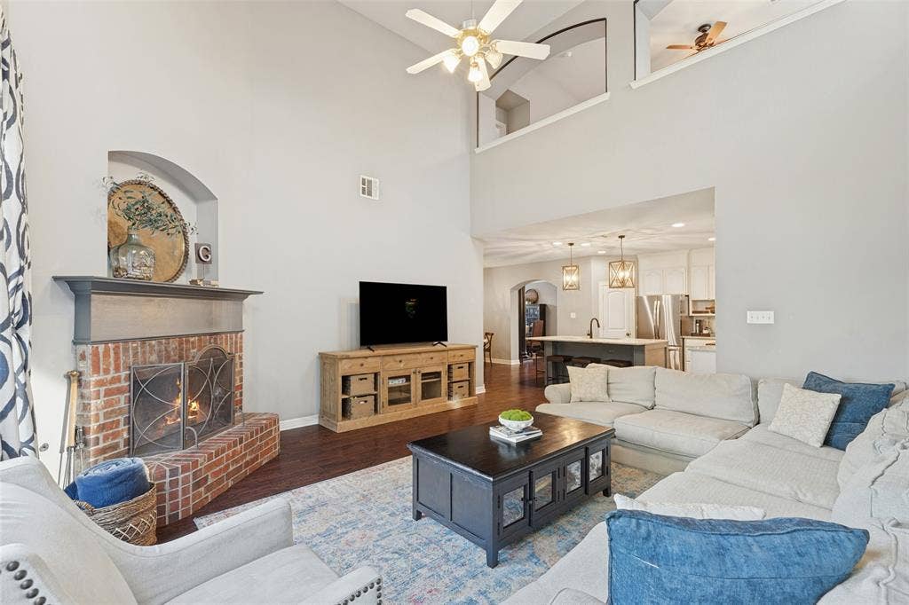 Living area featuring soaring vaulted ceilings, a full-height brick fireplace with a decorative arched niche, and dark wood-finish flooring