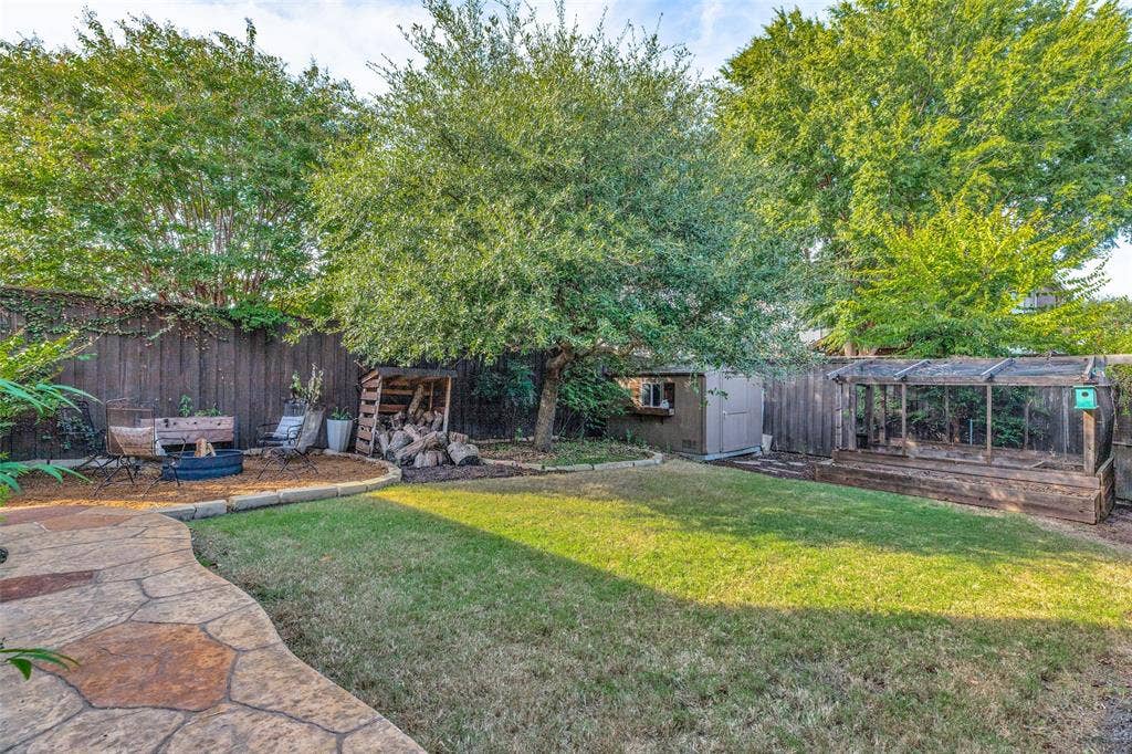 Backyard featuring stamped concrete, hardscaping, manicured lawn, perimeter wood fencing, mature trees, and a built-in outdoor storage structure