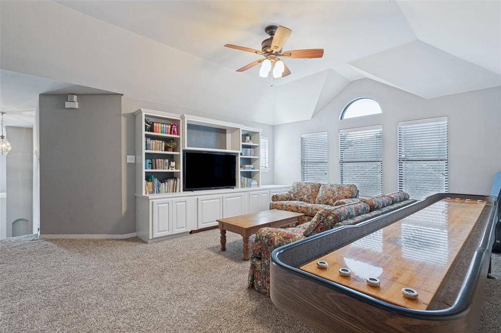 Vaulted ceiling, built-in white cabinetry, arched window, and ceiling fan