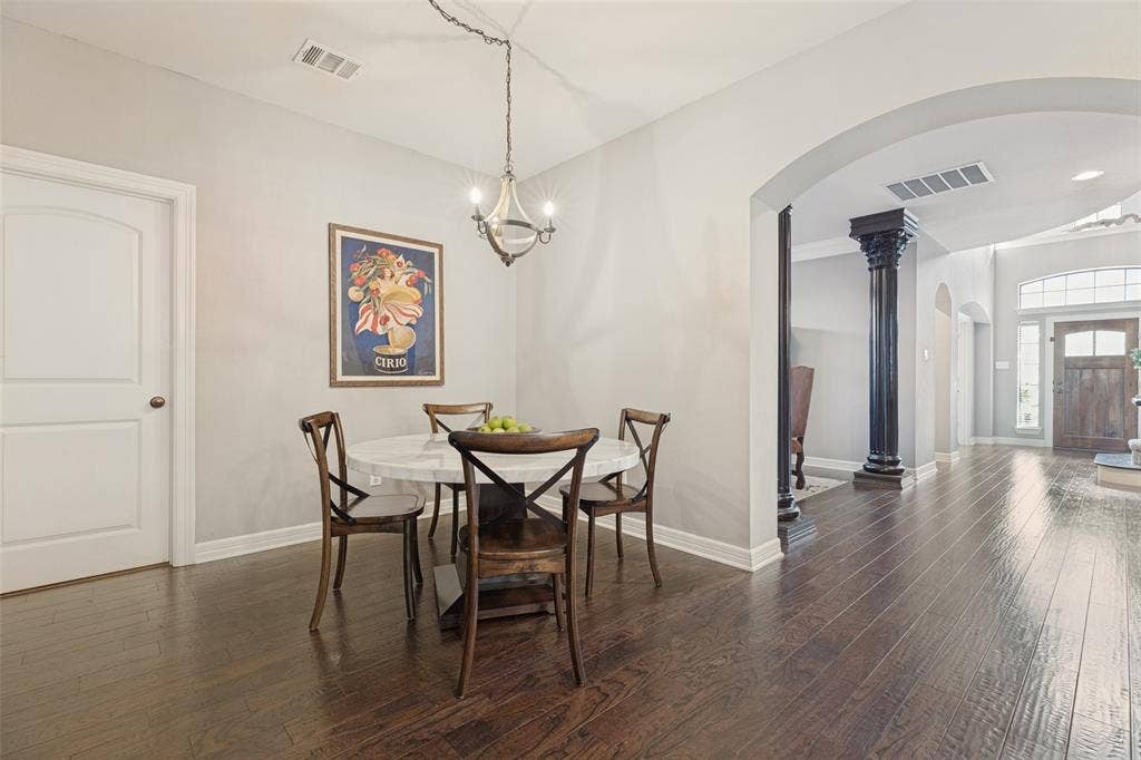 Wood-finish flooring, decorative column, arched entryway, and suspended multi-bulb light fixture